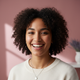 A close-up portrait of a smiling young adult, diverse, with natural lighting and a soft rose background.